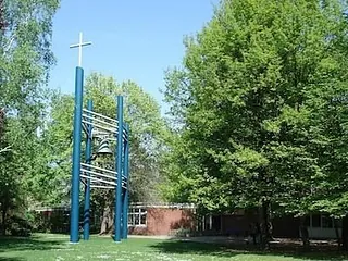 Blaue Glockenstruktur mit Kreuz zwischen Bäumen.