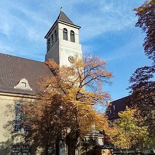 Alt Text: Kirchengebäude mit hohem Turm, umgeben von Herbstbäumen.