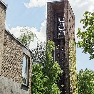 Moderner Kirchenglockenturm mit freiliegenden Glocken, umgeben von Grün.