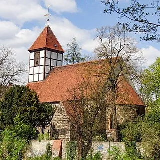 Alt Text: Historische Kirche mit rotem Dach und Fachwerkturm, umgeben von Bäumen.